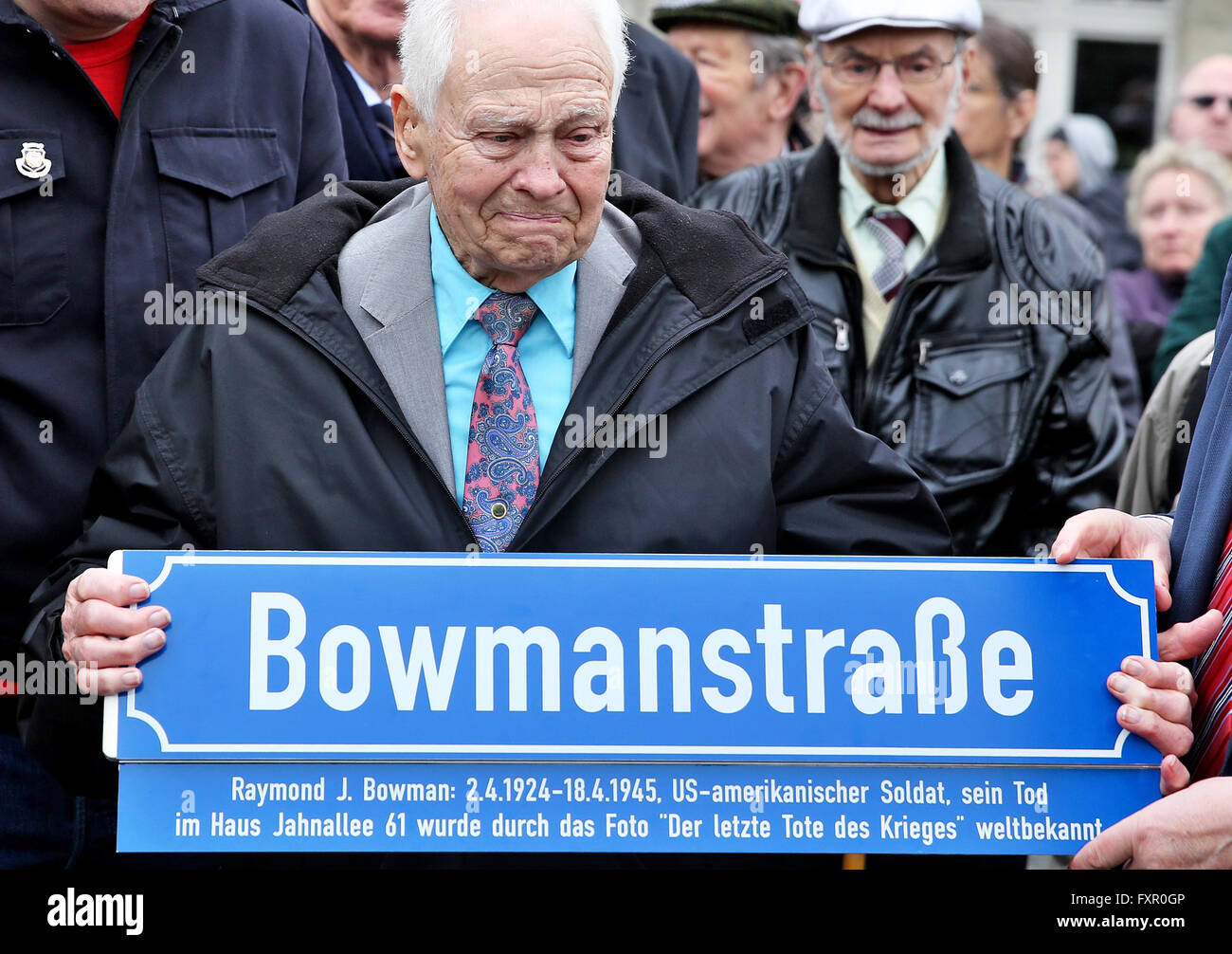US veteran Lehman Riggs holds up a sign for a street named after his dead comrade Bowman in front of the Capa House in Leipzig, Germany, 17 April 2016. The building, now also known as Capa House, became famous internationally through the picture 'Last man to die' by US war photographer Robert Capa. He documented how US soldier Raymond J. Bowman was shot dead on the second floor balcony on 18 April 1945 as US forces liberated Leipzig. The building was overhauled after years of decay, with an exhibition now showcasing the history of the building. Photo: JAN WOITAS/dpa Stock Photo
