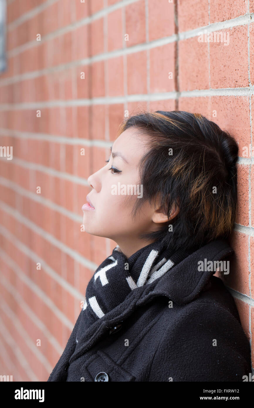 Asian American Woman Leaning Against Brick Wall Stock Photo