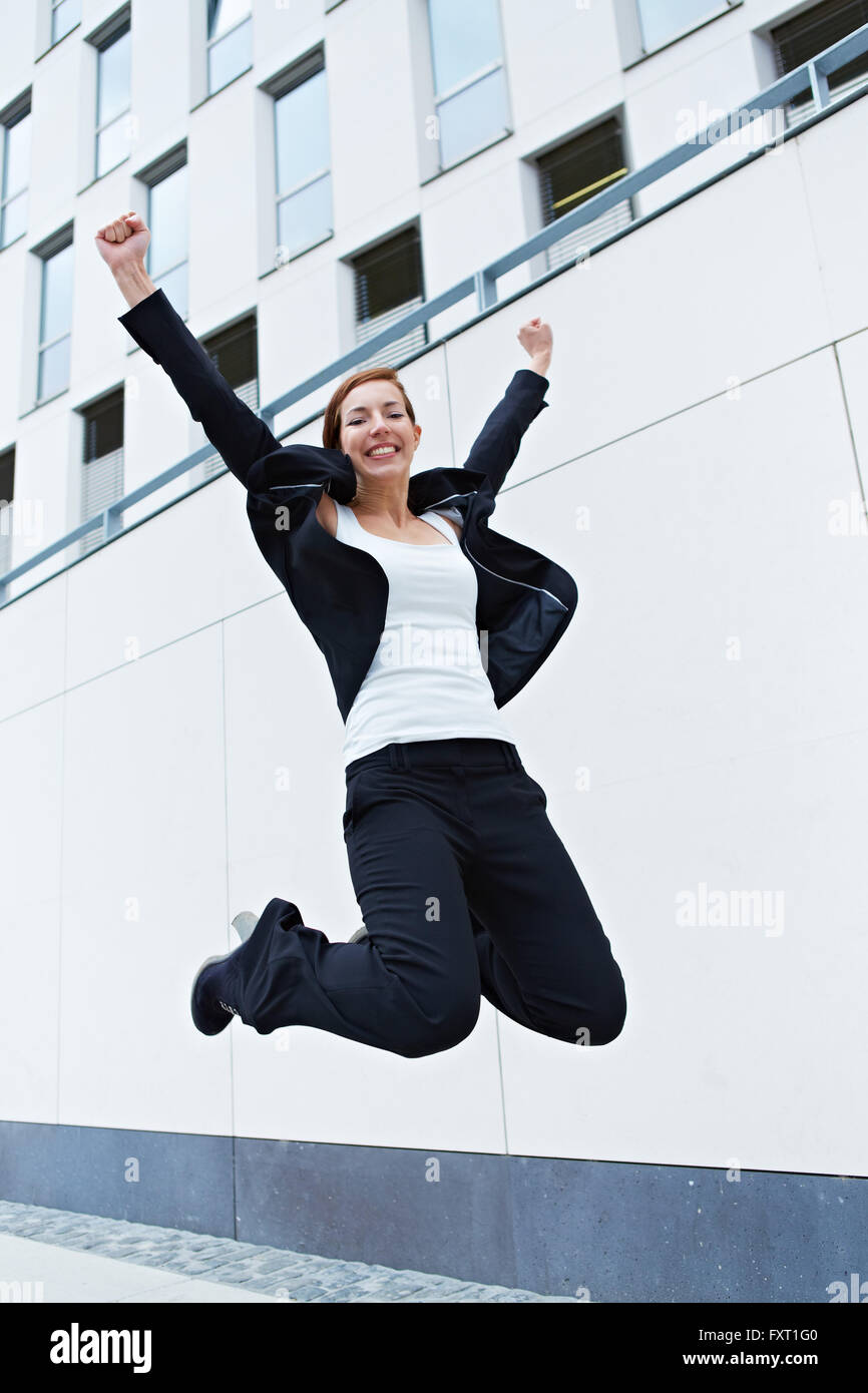 Happy business woman jumping into the air in front of office building Stock Photo