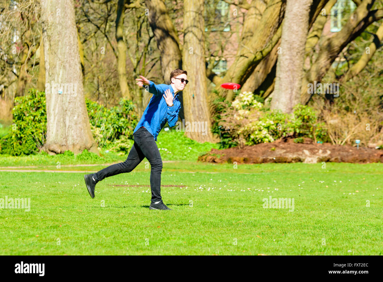 Lund, Sweden - April 11, 2016: Everyday city life. Young adult man in a park is throwing a flying disc. He is making an effort, Stock Photo