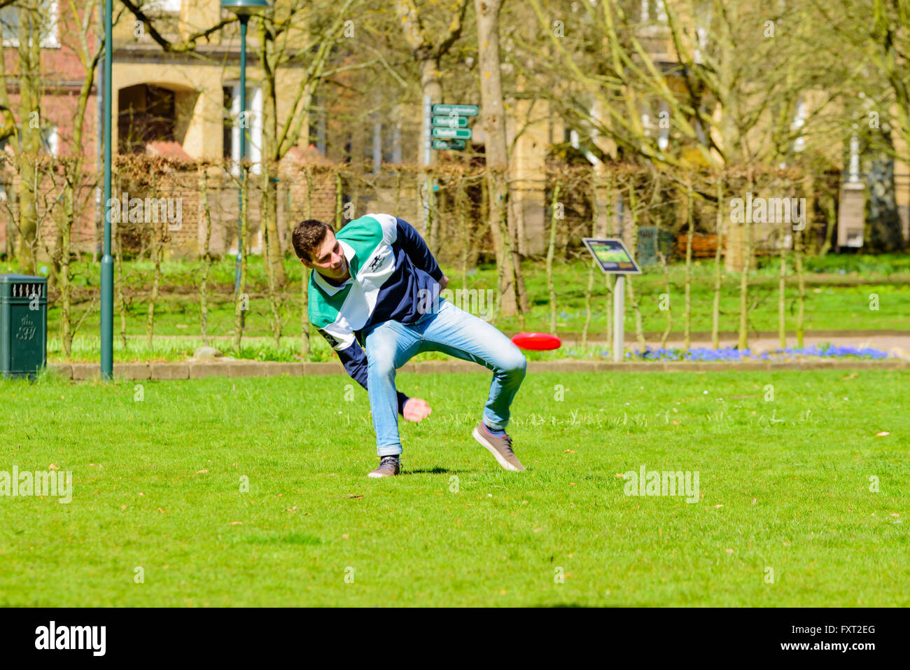 Lund, Sweden - April 11, 2016: Everyday city life. Young adult man in a park is throwing a flying disc between his legs. Stock Photo