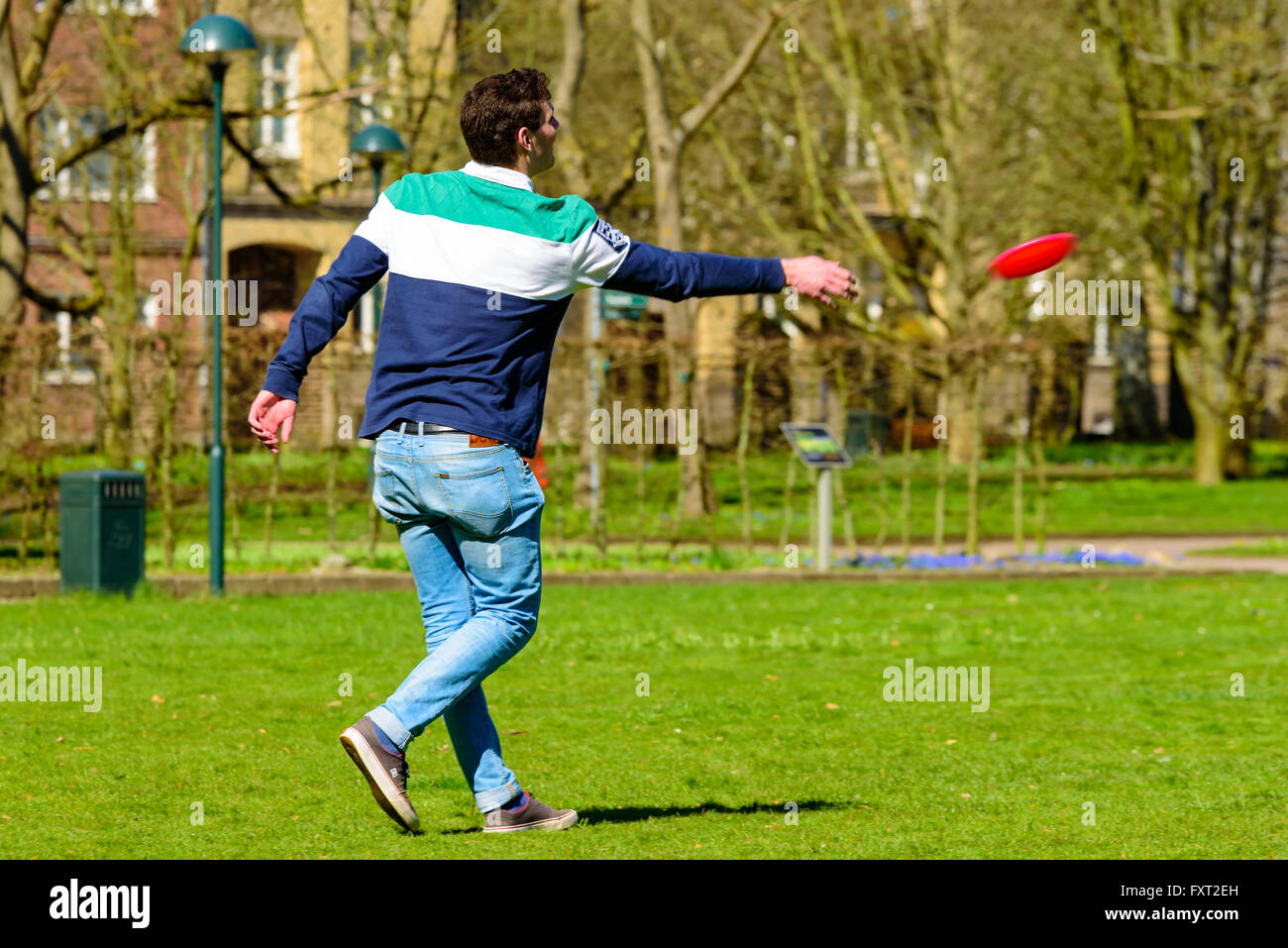 Lund, Sweden - April 11, 2016: Everyday city life. Young adult man in a park is throwing a flying disc to the side. Stock Photo