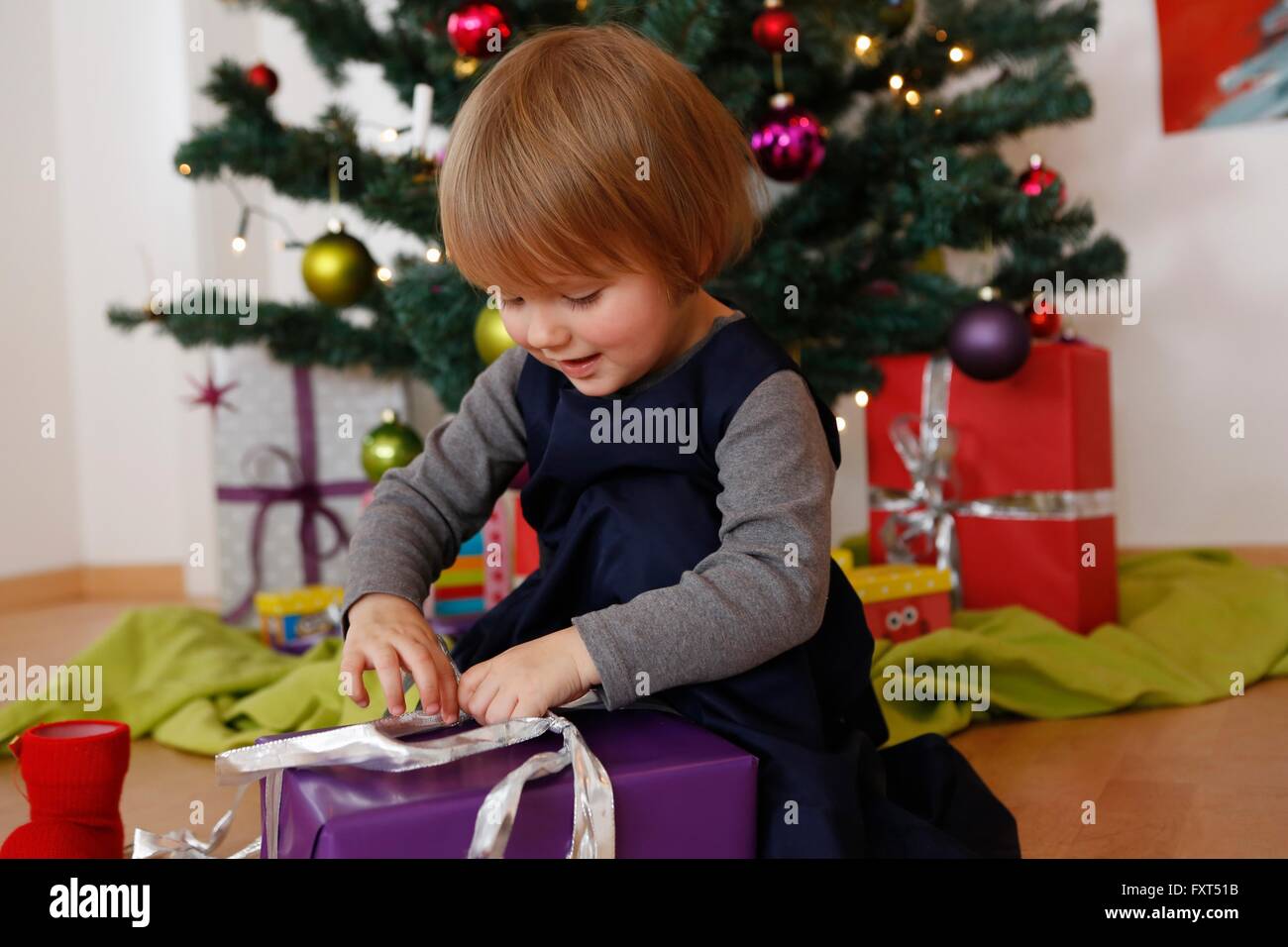 Girl in front of christmas tree looking down opening gifts Stock Photo