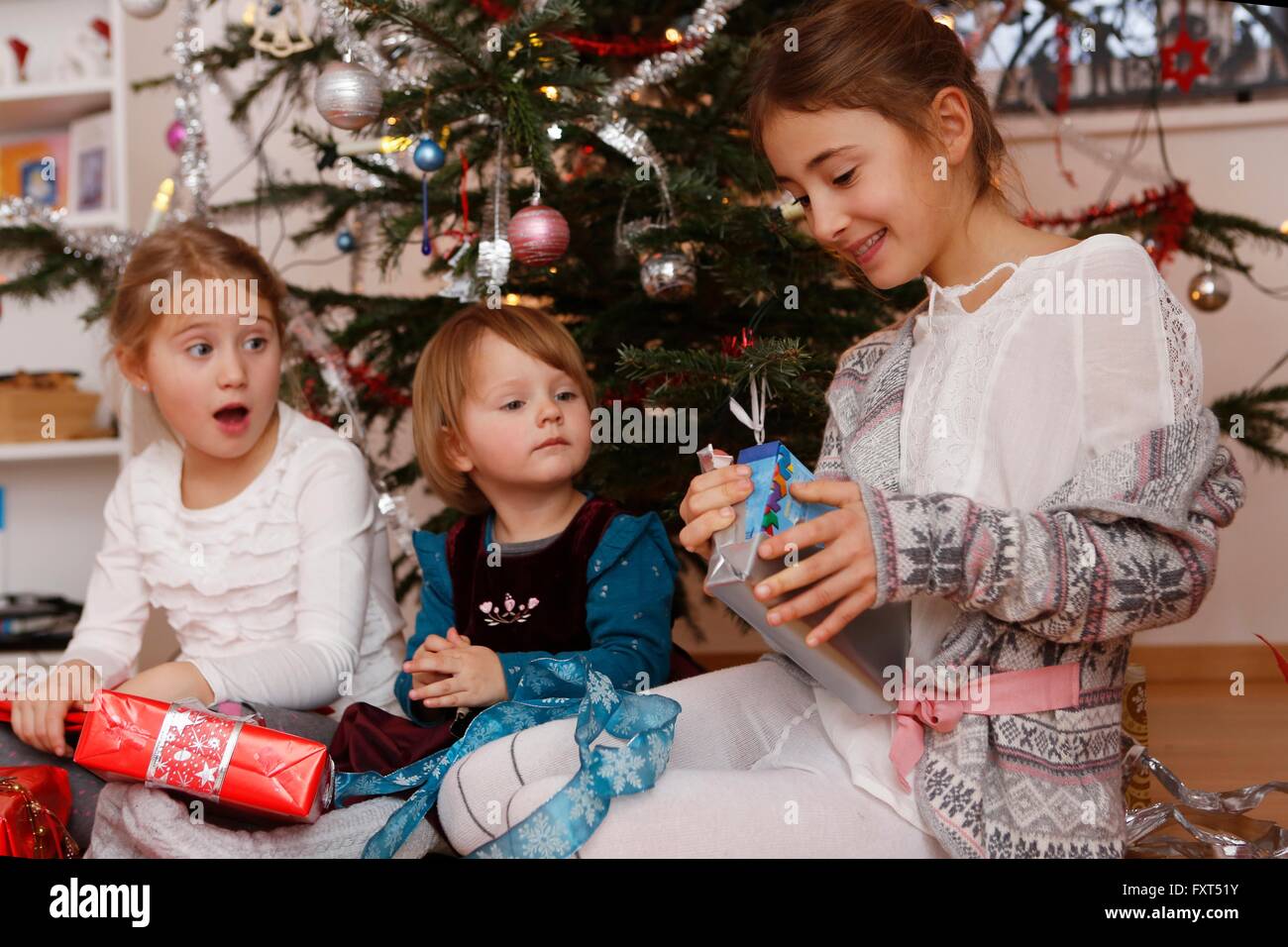 Girls in front of christmas tree opening gifts Stock Photo