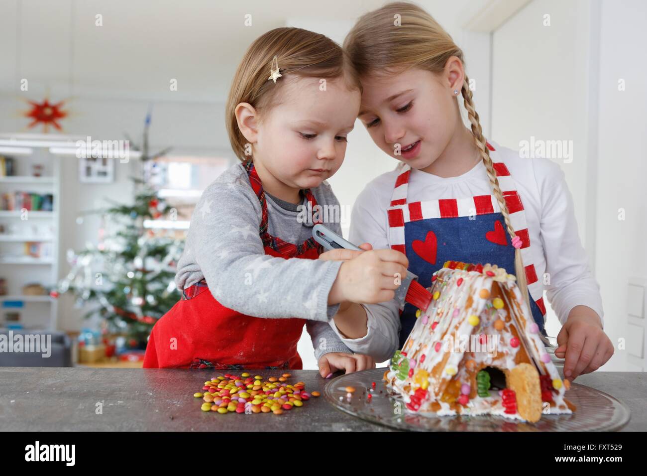 Girls at kitchen counter decorating gingerbread house together Stock Photo