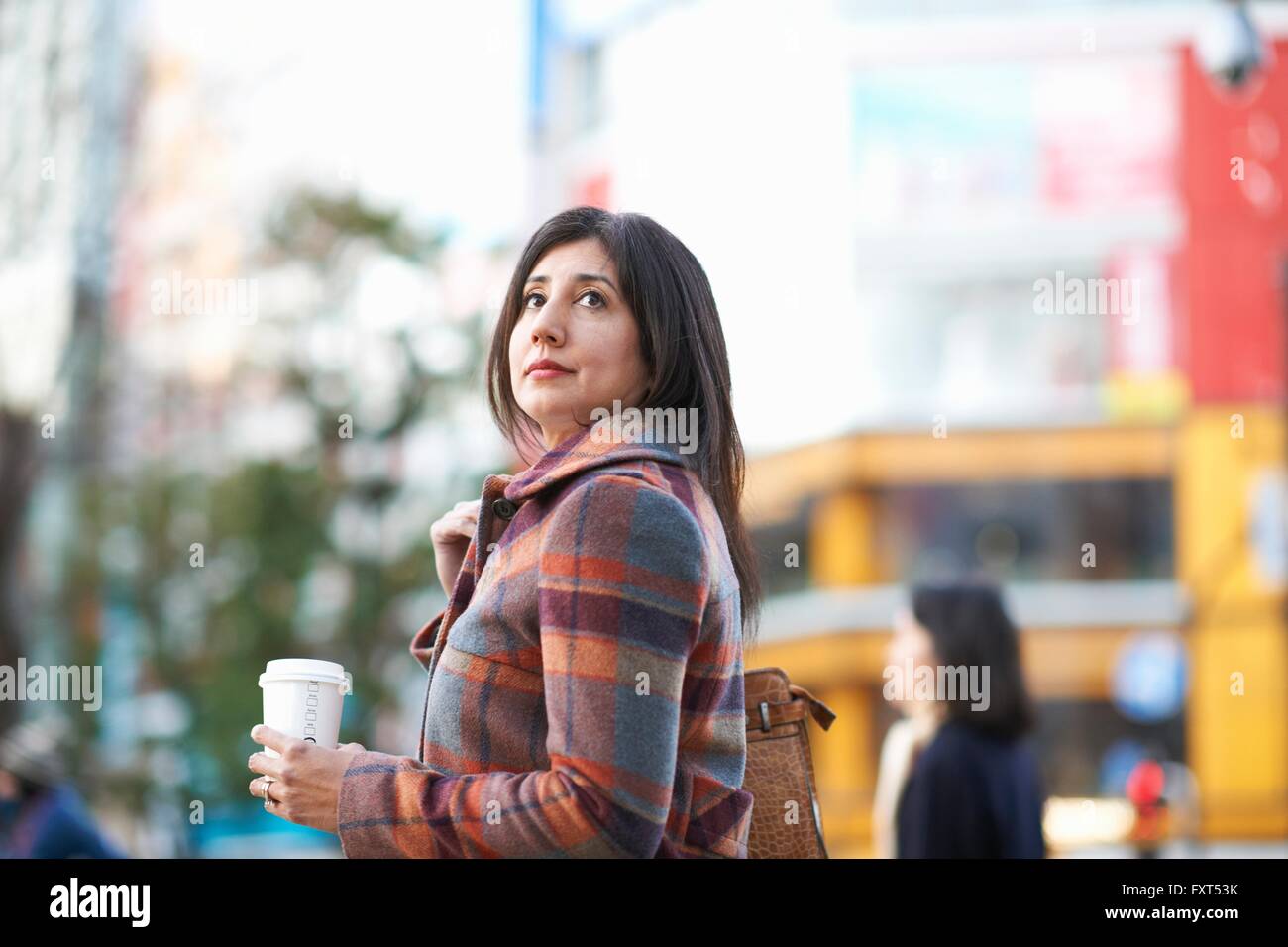 Mature female tourist with takeaway coffee on city street, Tokyo, Japan Stock Photo