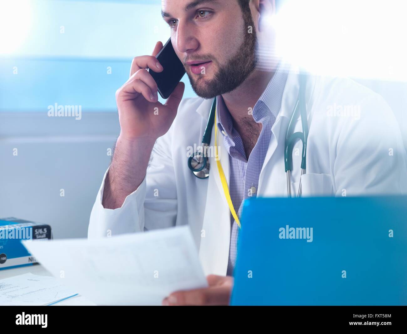 Junior doctor using smartphone whilst reviewing medical records in clinic Stock Photo