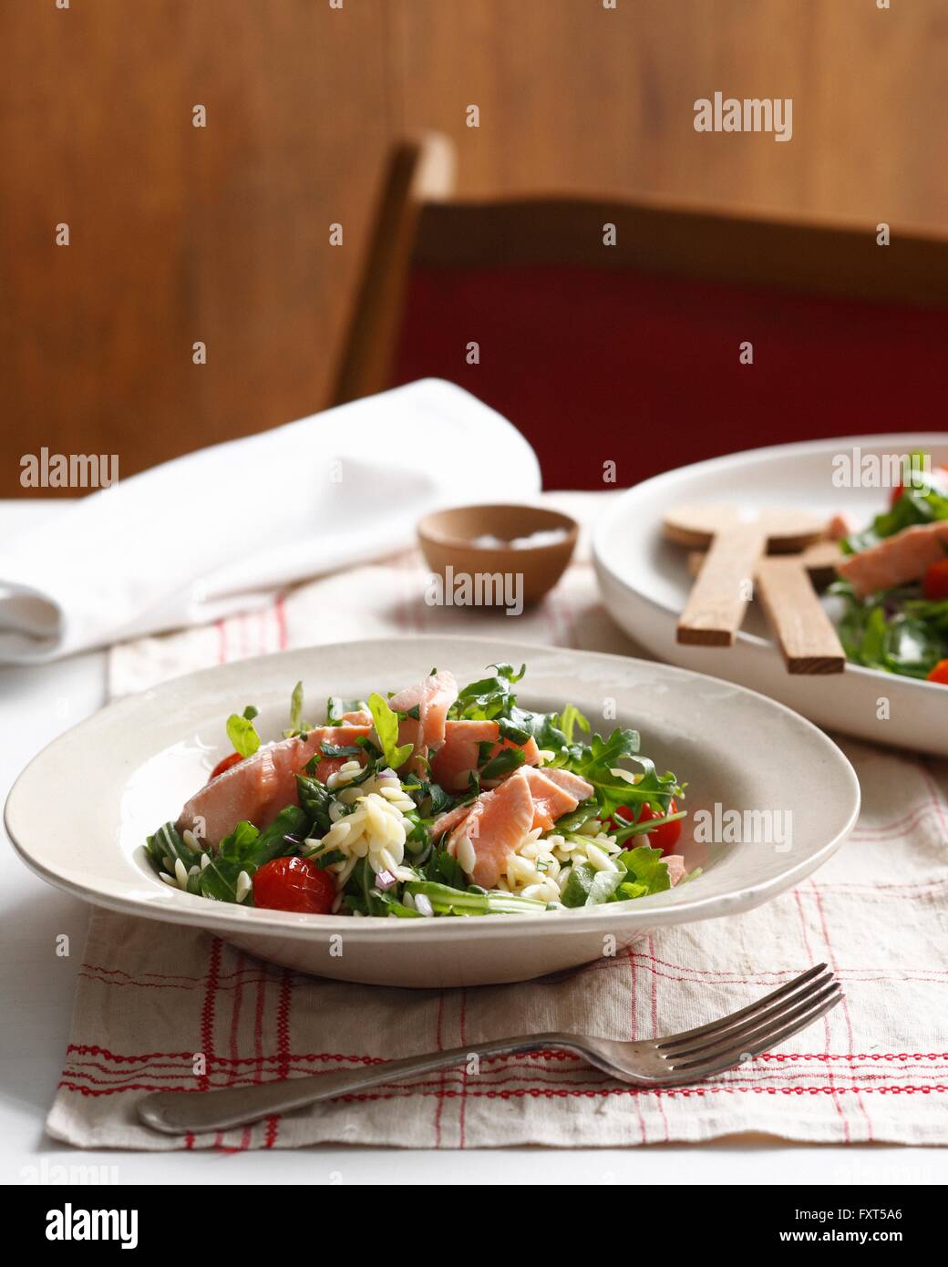 Bowl of poached salmon orzo with cherry tomatoes and rocket Stock Photo