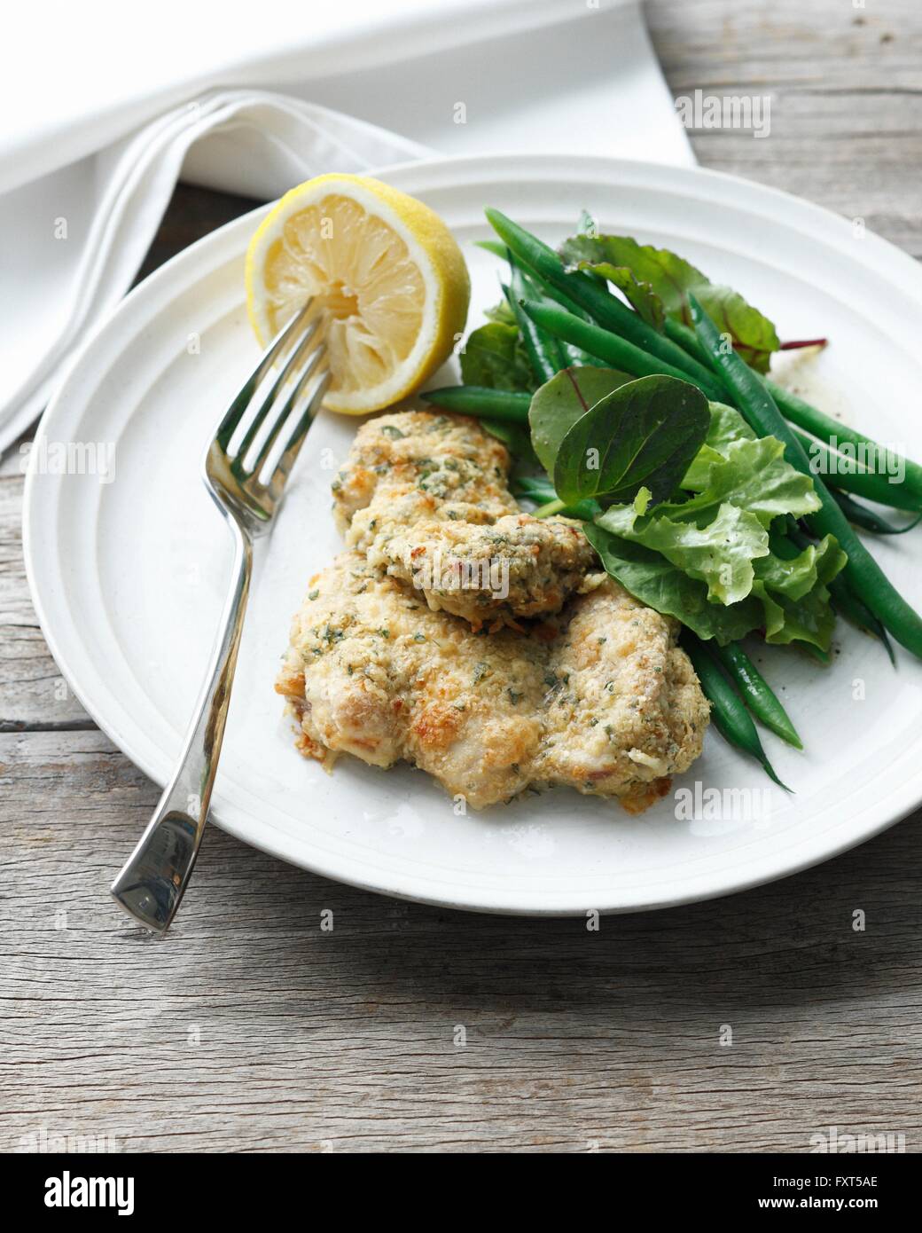 Plate of wholemeal chicken with crusted chicken pieces, green beans, mesclun salad and lemon Stock Photo