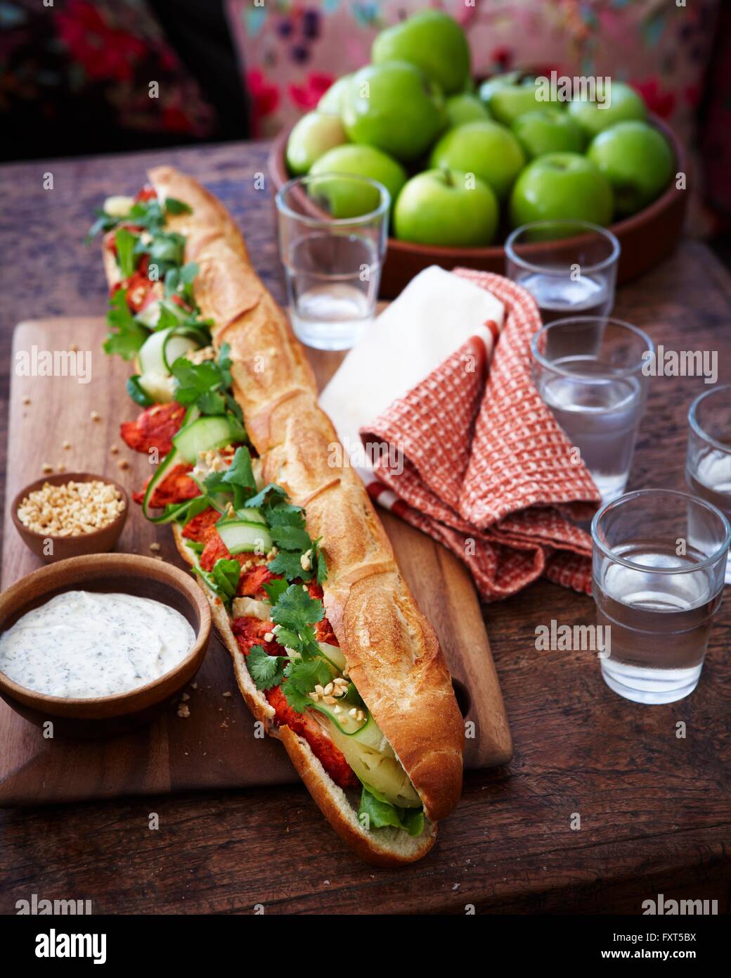 Tandoori chicken baguette and glasses of water on wooden table Stock Photo