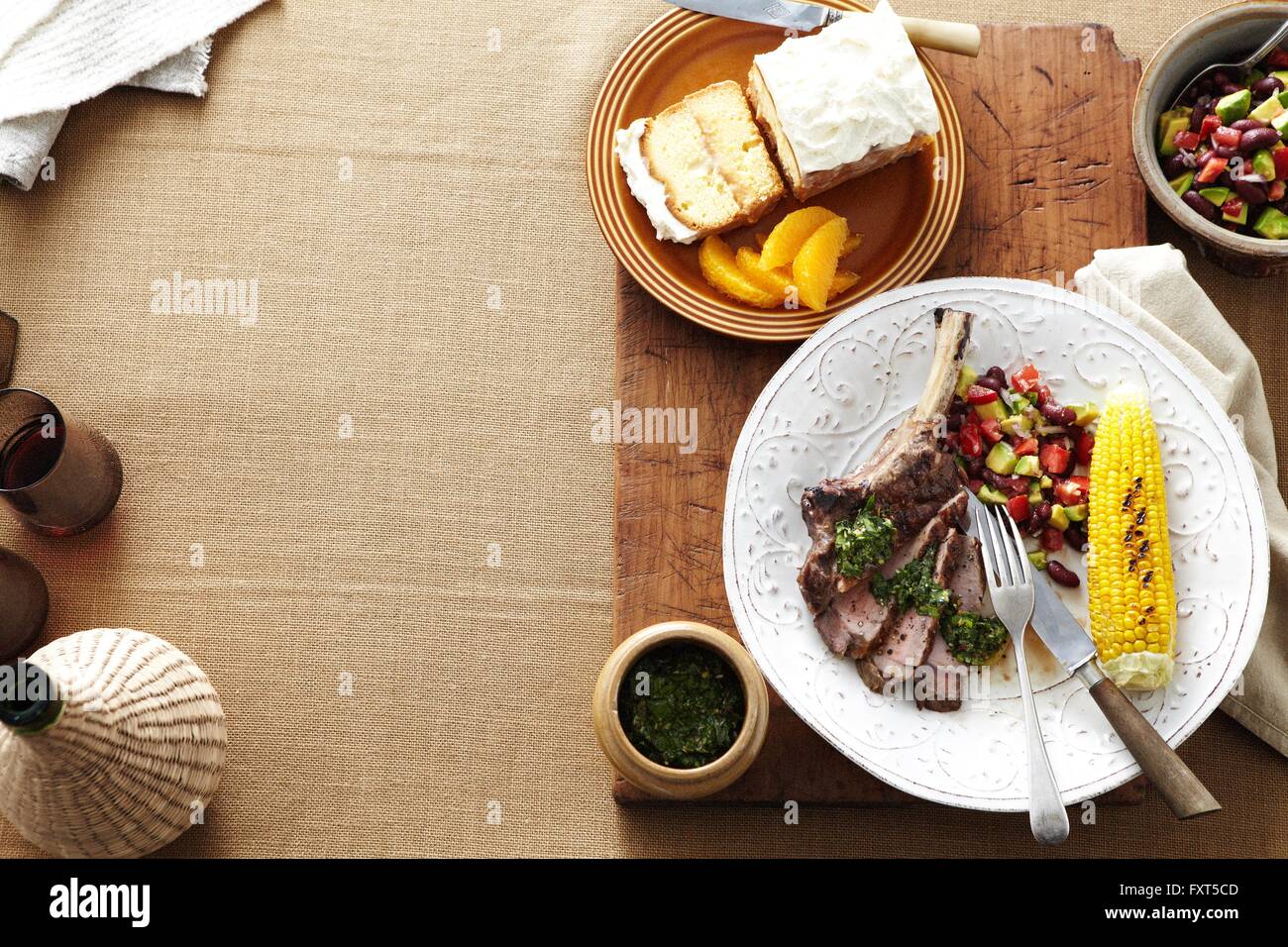 Overhead view of South American dinner with plate of steak, corn, kidney bean salad and salsa verde Stock Photo