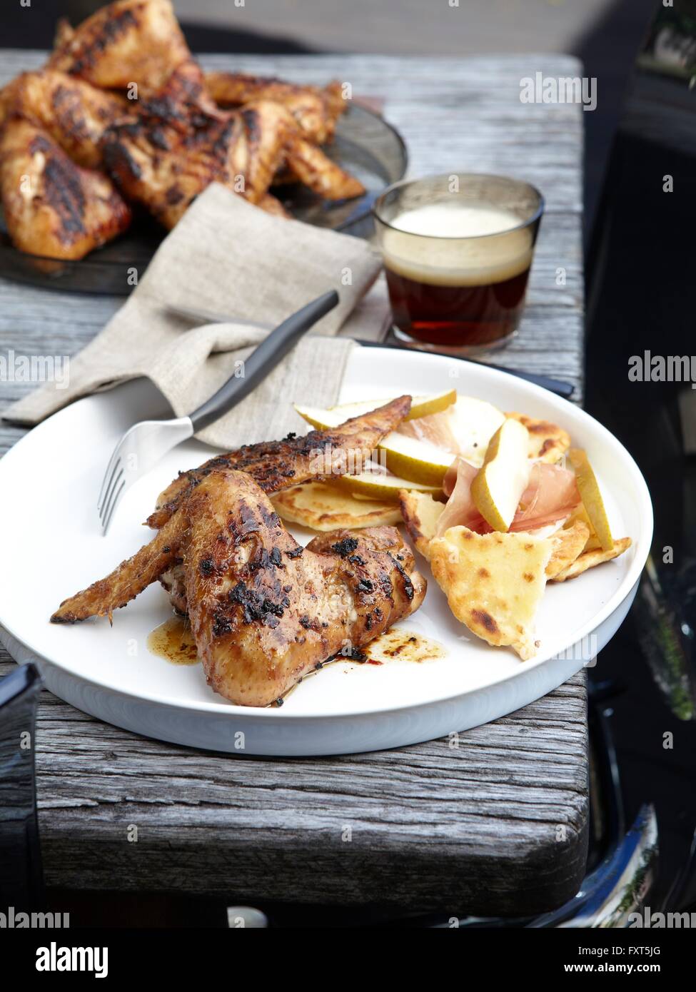 Barbecued spicy chicken wings with tumbler of beer Stock Photo