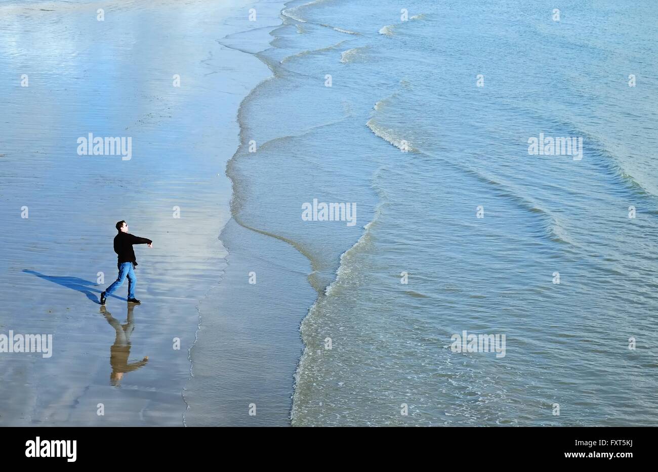 High angle side view of mature man on beach throwing stones into ocean Stock Photo