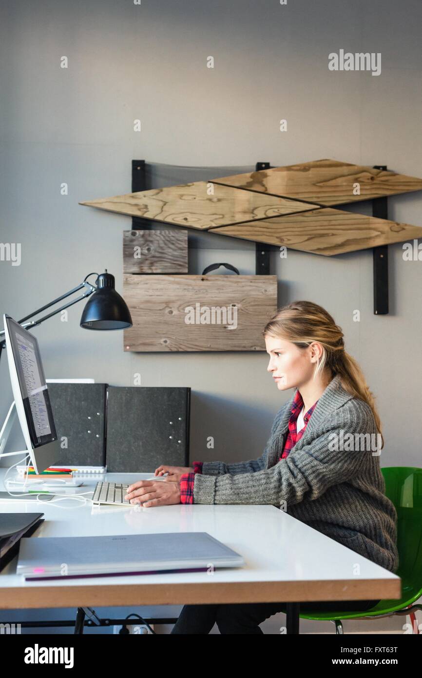 Side view of young woman in office sitting at desk using computer Stock Photo