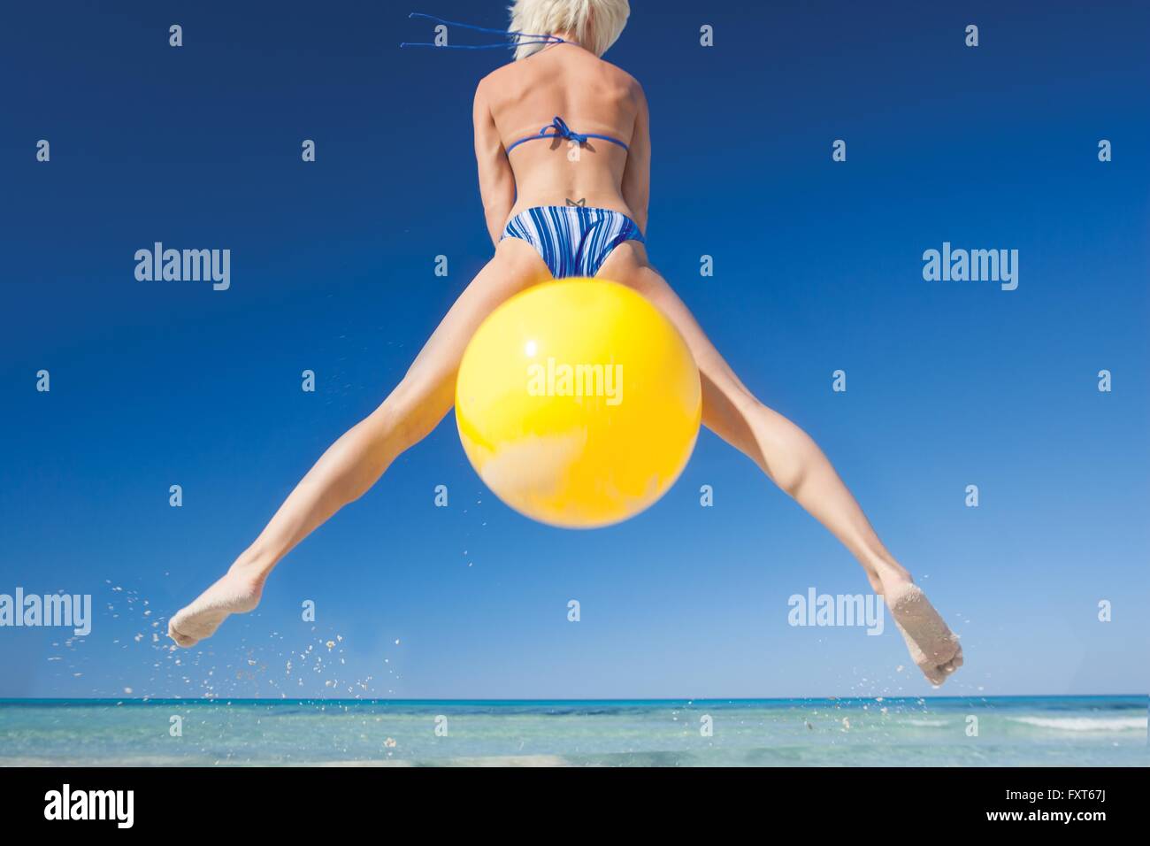 Rear view of young woman jumping mid air on space hopper at beach, Majorca, Spain Stock Photo