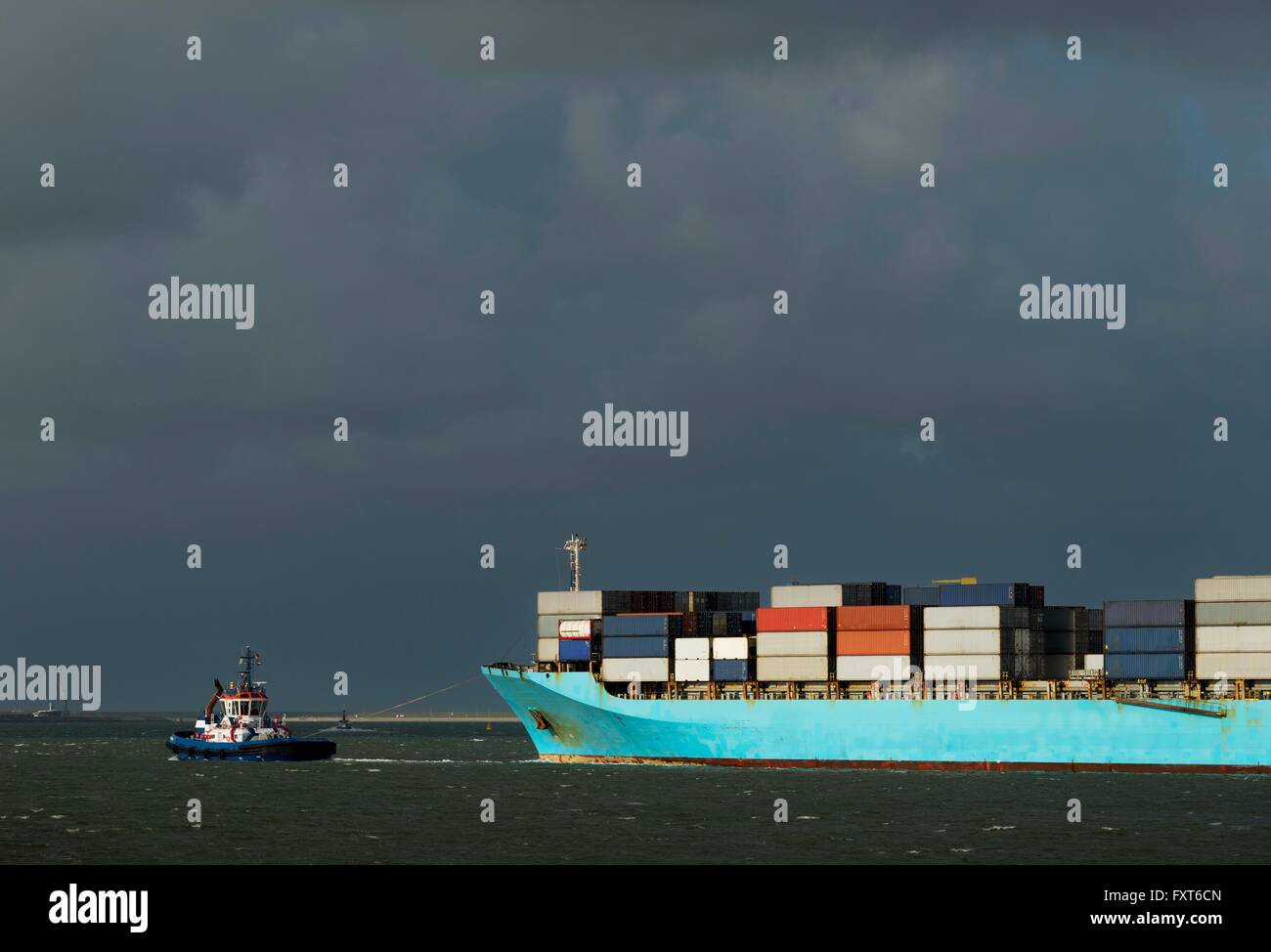 Container ship entering Rotterdam harbour with help of tug boat Stock Photo
