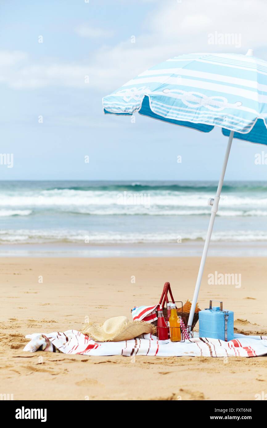 Sunhat, cool box and picnic basket on beach towel underneath parasol on beach Stock Photo