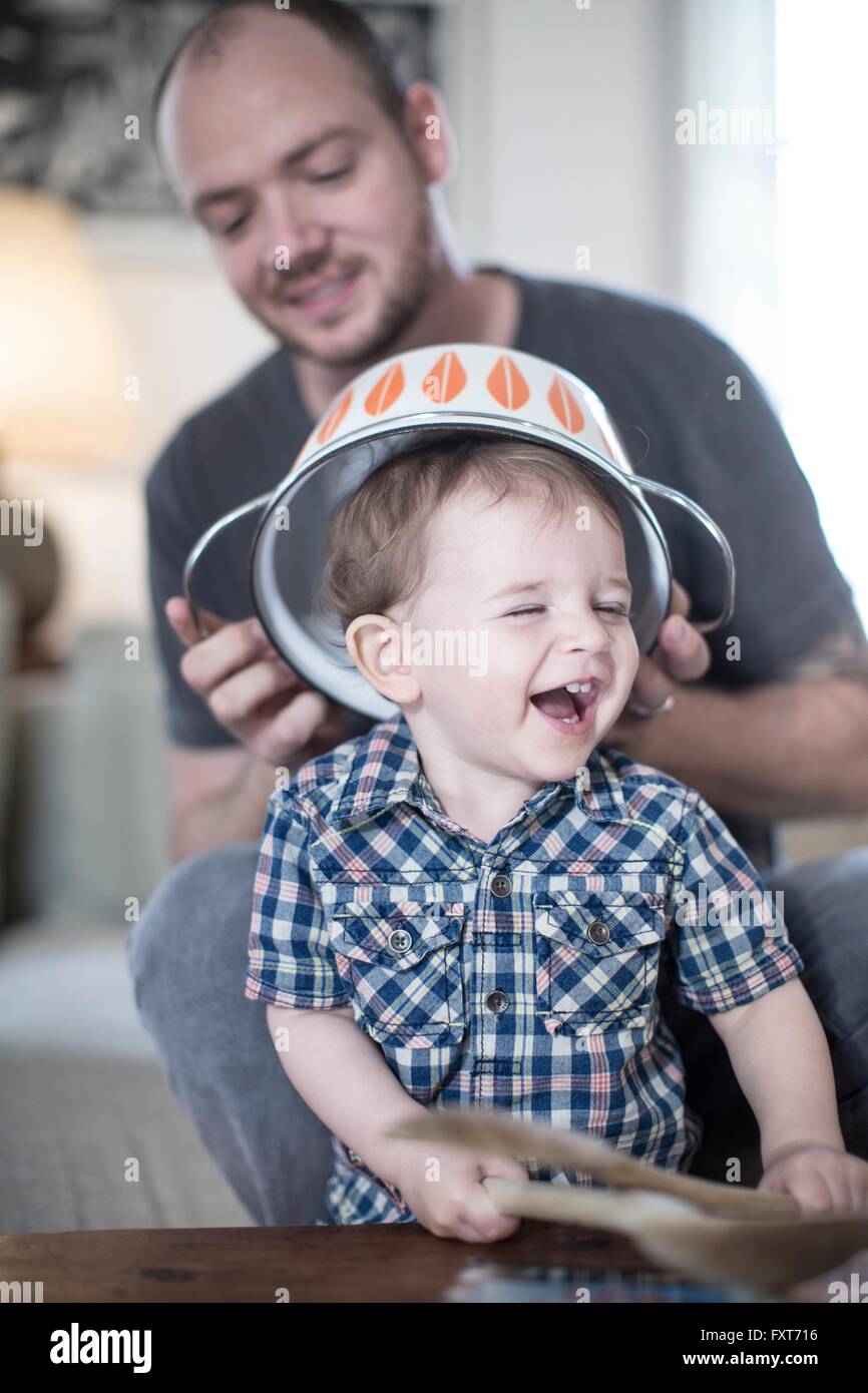Father placing colander on smiling baby boys head Stock Photo