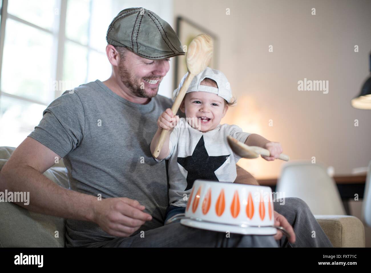 Baby boy on fathers lap playing drums on upside down saucepan Stock Photo