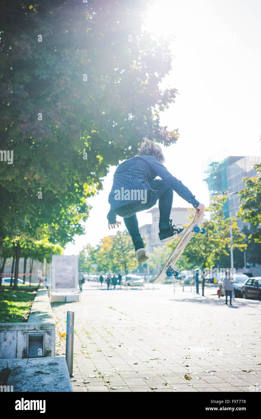 Young male skateboarder doing skateboarding jump on sidewalk Stock