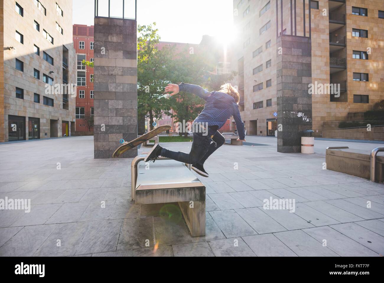 Young male skateboarder falling head first whilst skateboarding on urban concourse seat Stock Photo