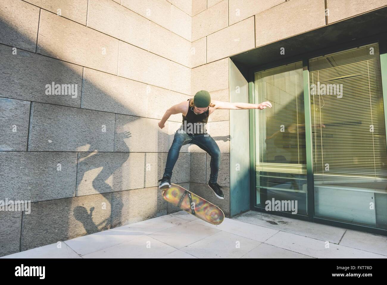 Young male urban skateboarder doing skateboarding jump trick in corner