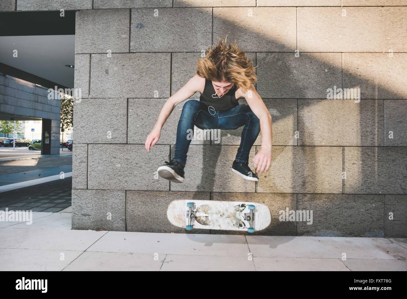 Young male urban skateboarder doing skateboarding jump trick above