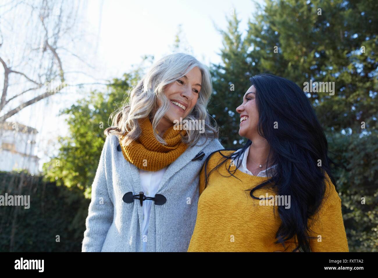 Women in garden arms around each other face to face smiling Stock Photo