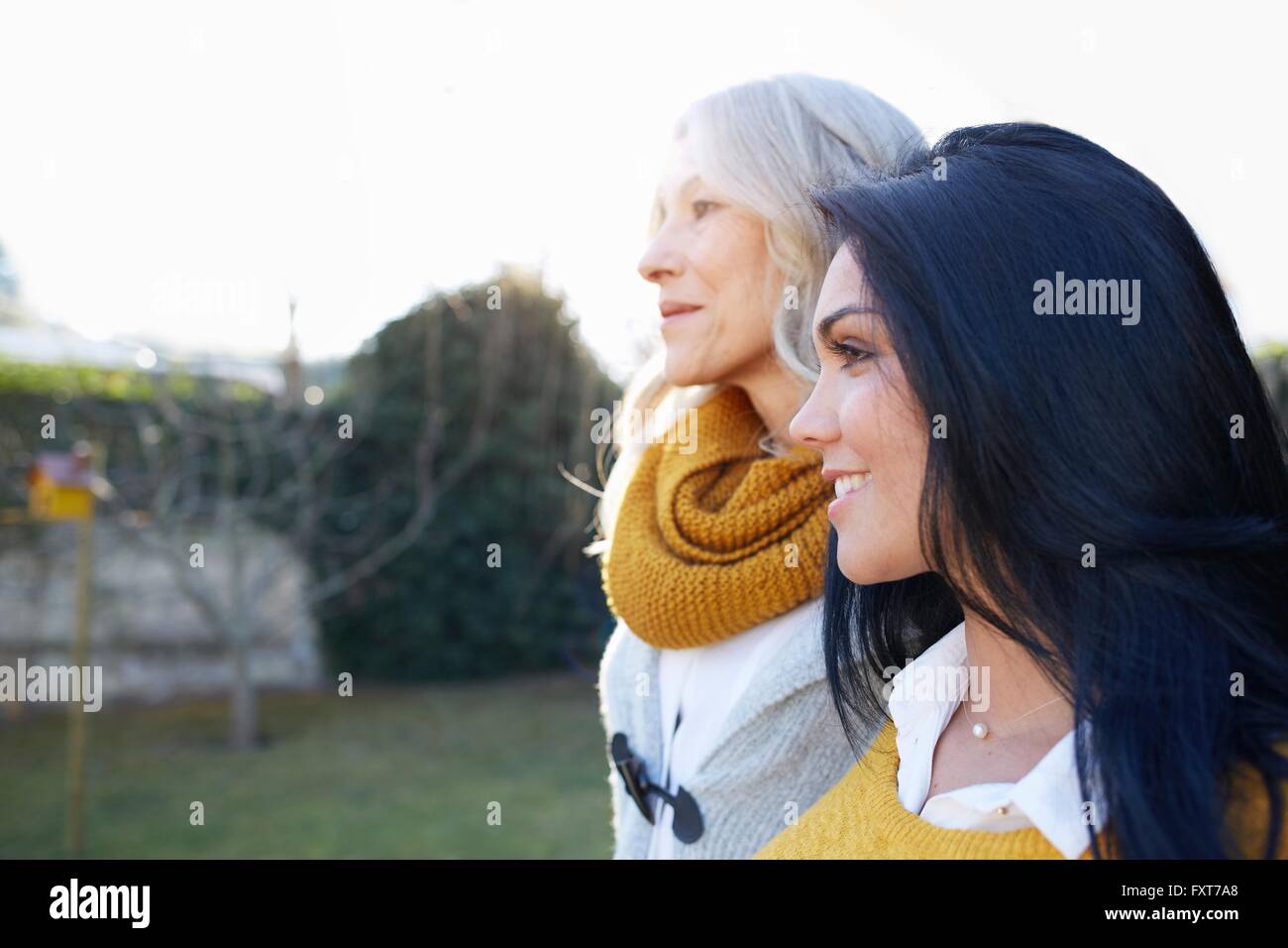 Women in garden arms around each other looking away smiling Stock Photo ...