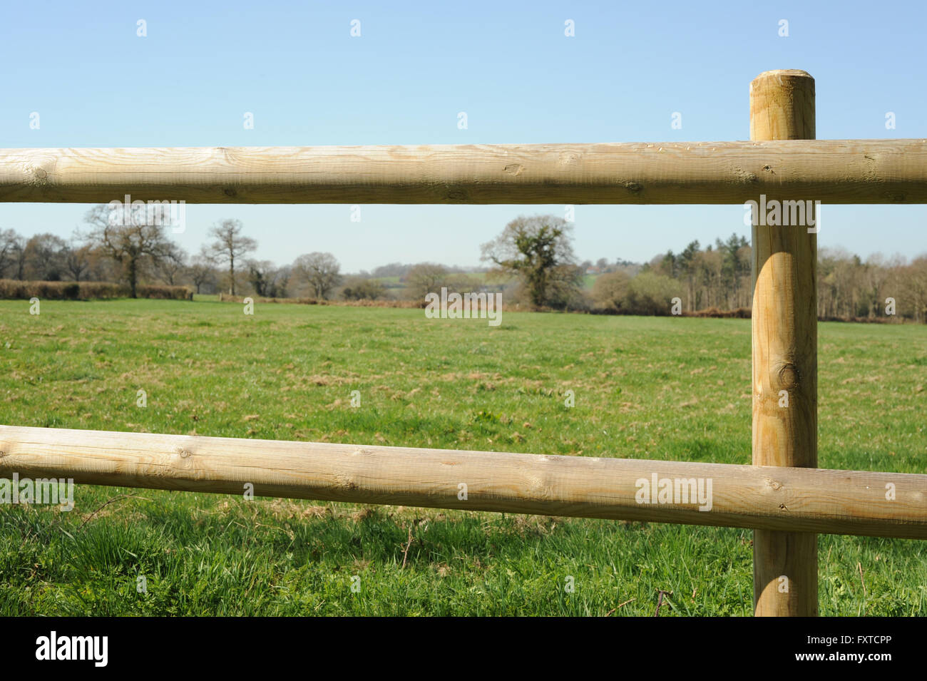 Photograph of a wooden post and rail with field and grass behind Stock Photo