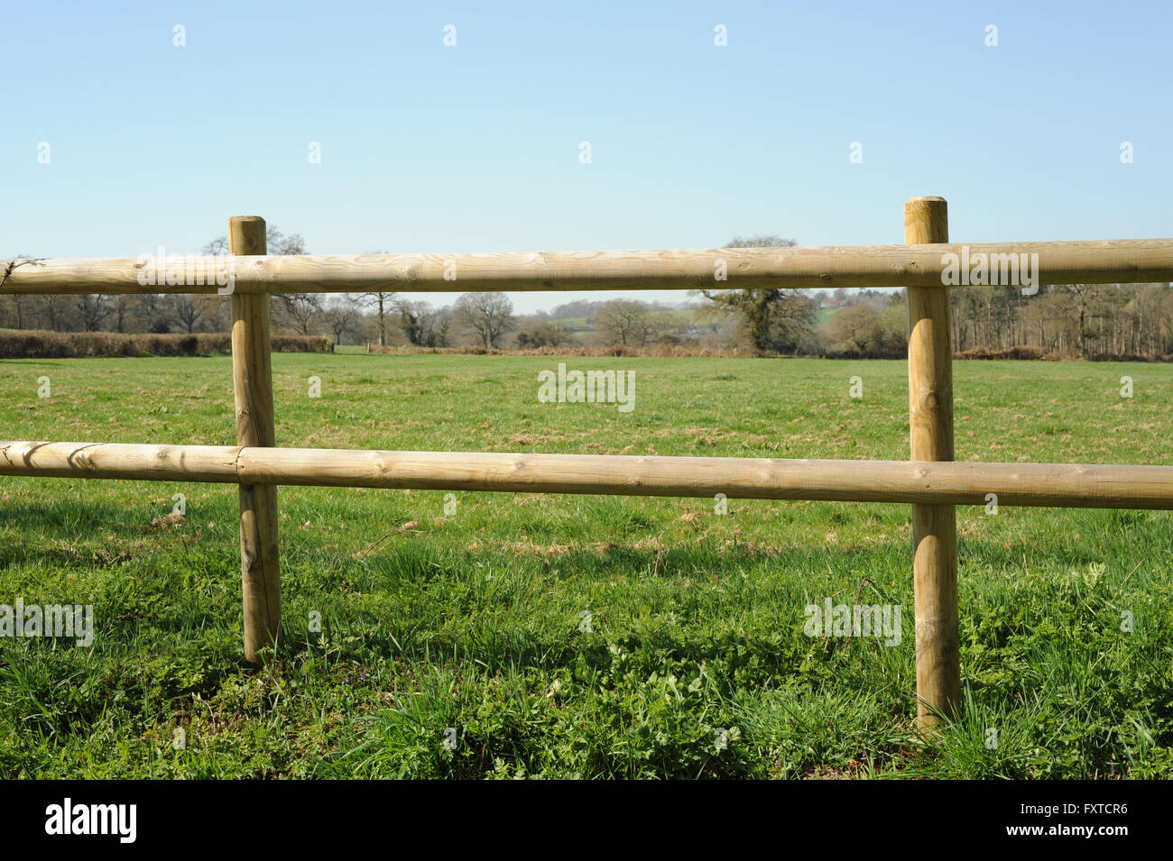 Photograph of a wooden post and rail with field and grass behind Stock Photo