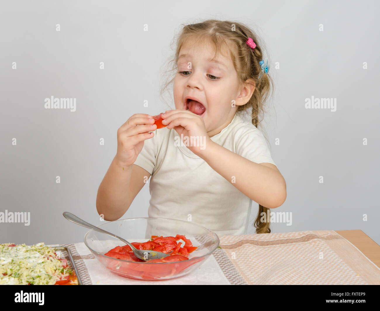 A little girl tries to stick to widely open mouth large slice of tomato Stock Photo