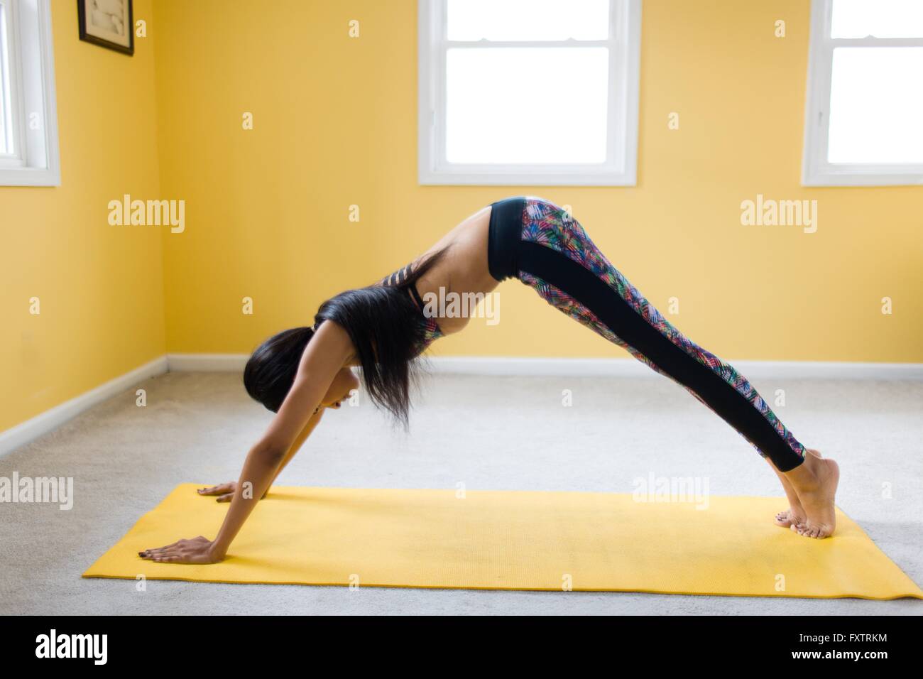 Young woman bending over in yoga pose on yoga mat Stock Photo