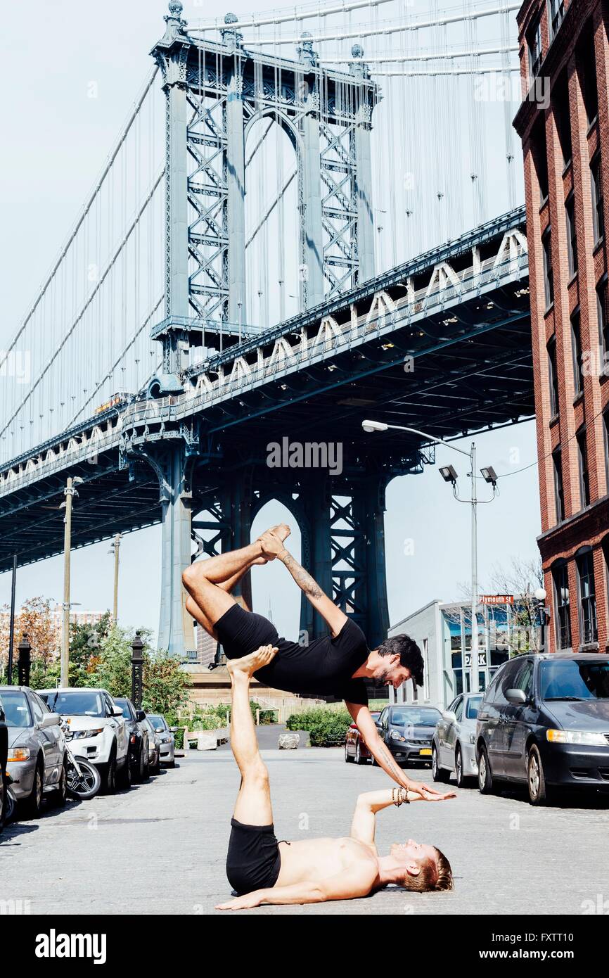 Man balancing on top of another in yoga position by Manhattan Bridge, New York, USA Stock Photo