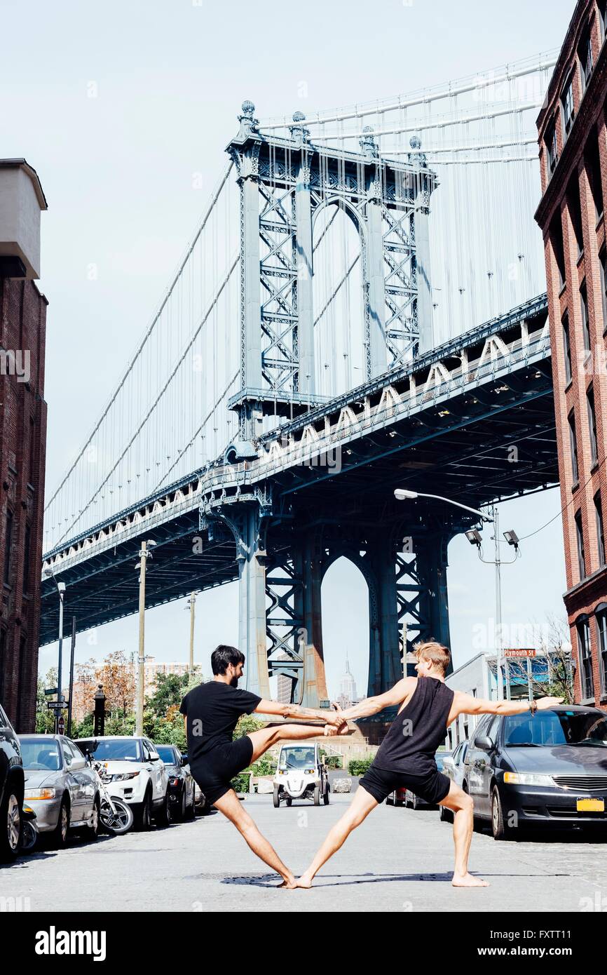 Two men leaning sideways in yoga position in front of Manhattan Bridge, New York, USA Stock Photo