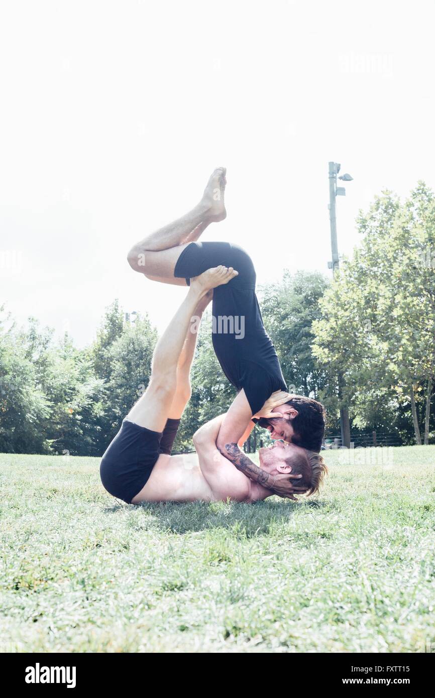 Two men poised in face to face yoga position in park Stock Photo