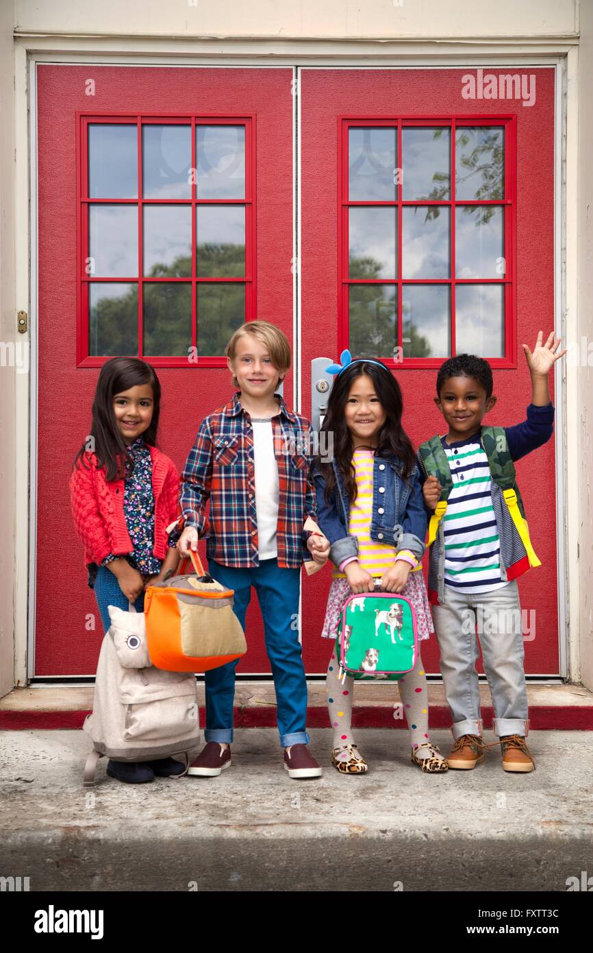 Portrait of elementary schoolgirls and boys waving from elementary school doorway Stock Photo