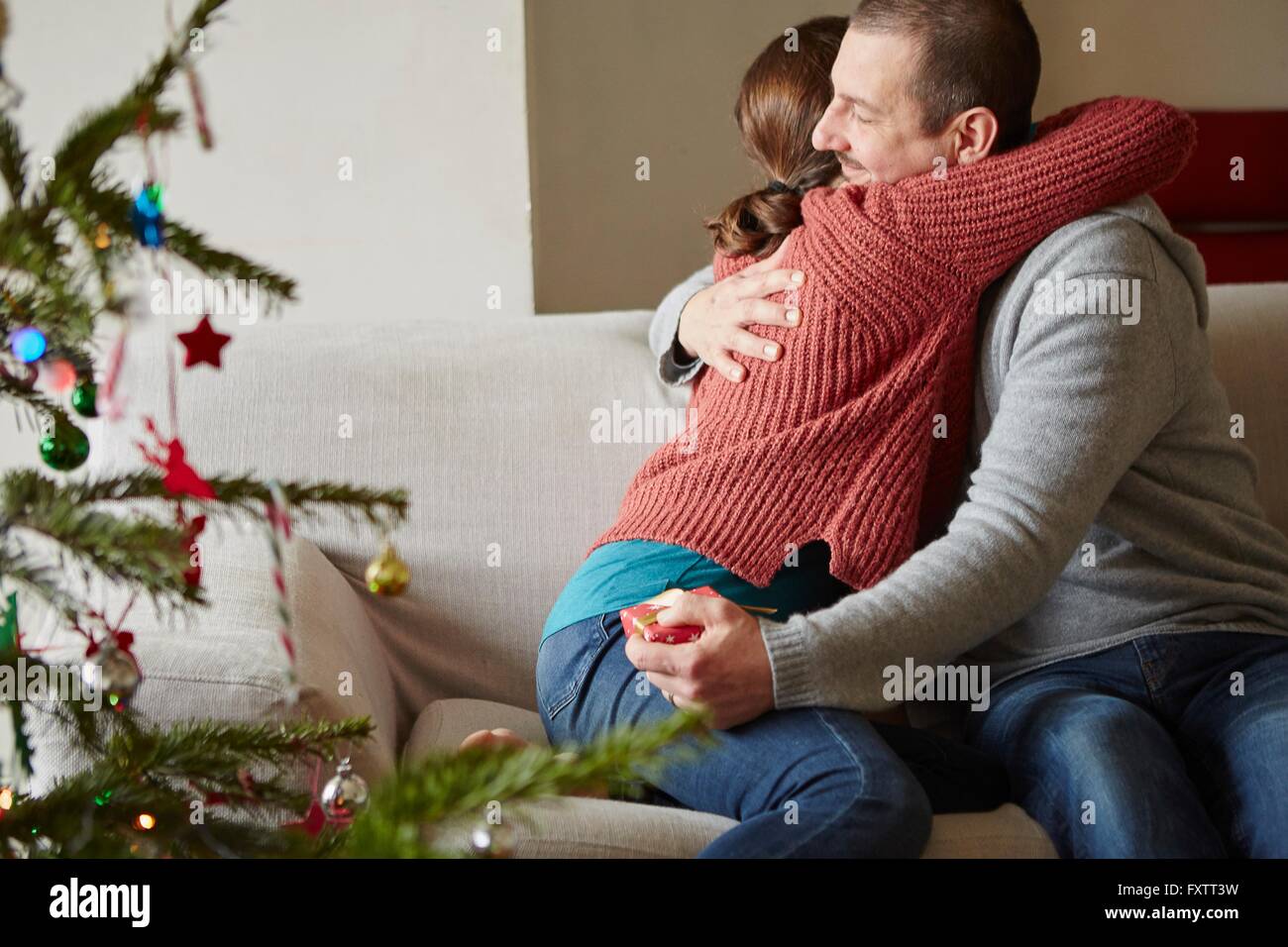 Couple holding xmas gift hugging on sofa at xmas Stock Photo