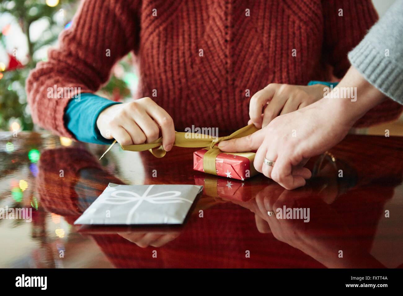 Cropped shot of couples hands wrapping xmas gift at table Stock Photo