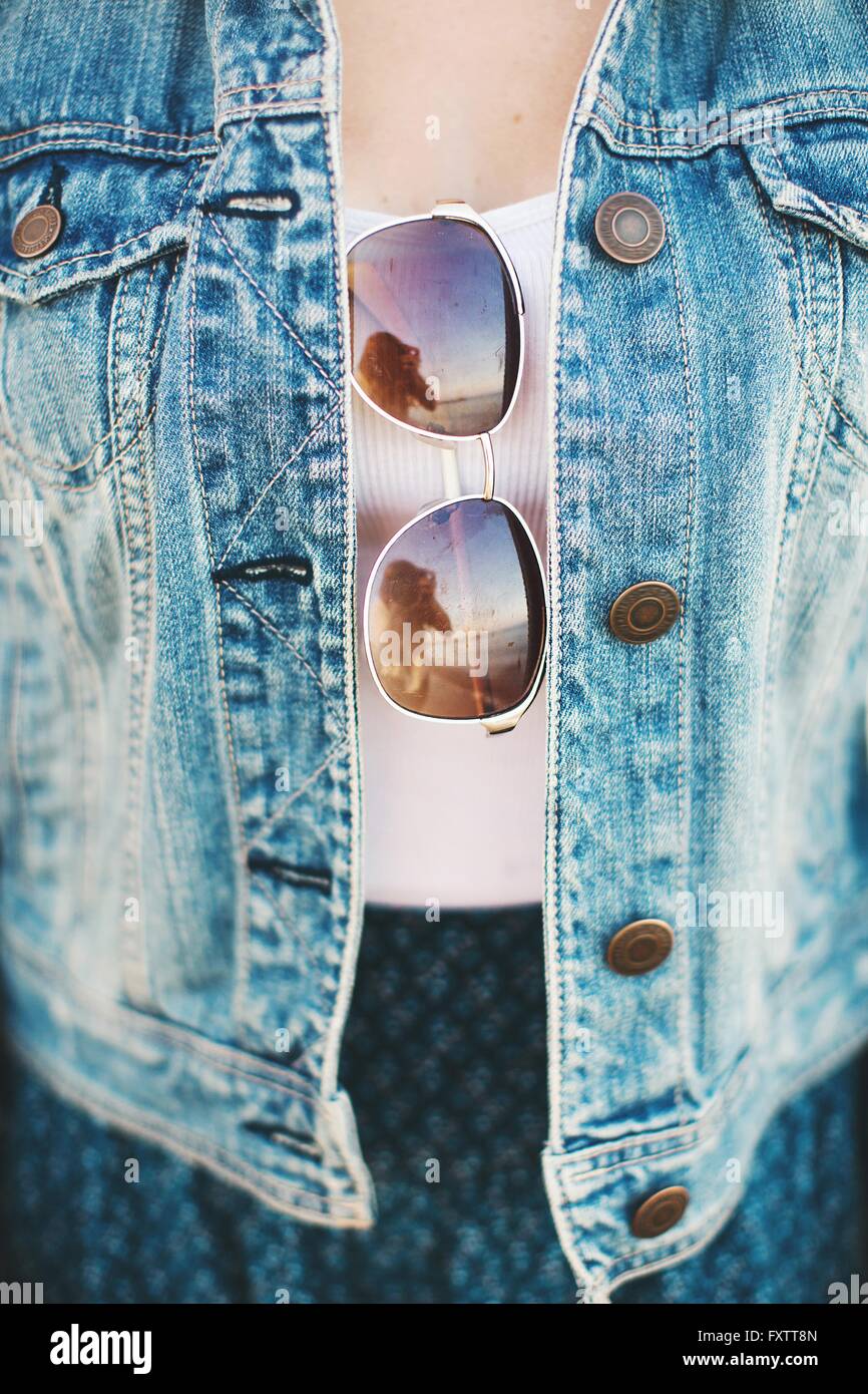 Cropped view of woman mid section wearing denim jacket with sunglasses hanging from top Stock Photo