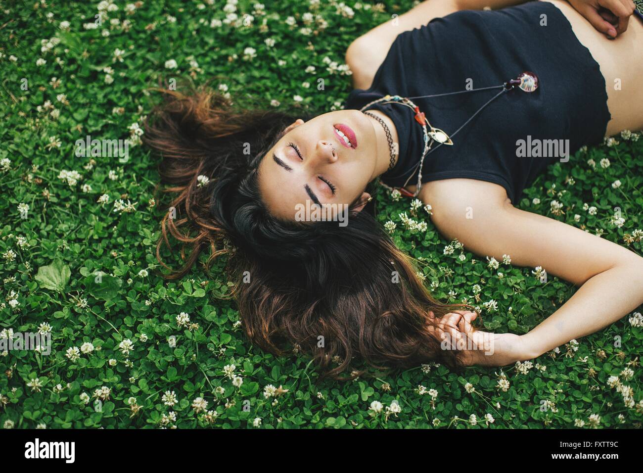 High angle view of woman with nose ring lying on clover covered grass, eyes closed Stock Photo