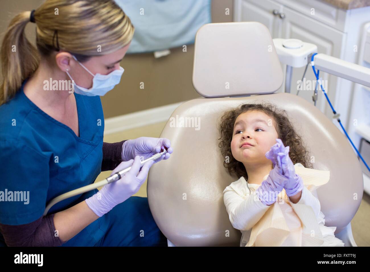 Girl in dental chair watching dentist prepare dental equipment Stock