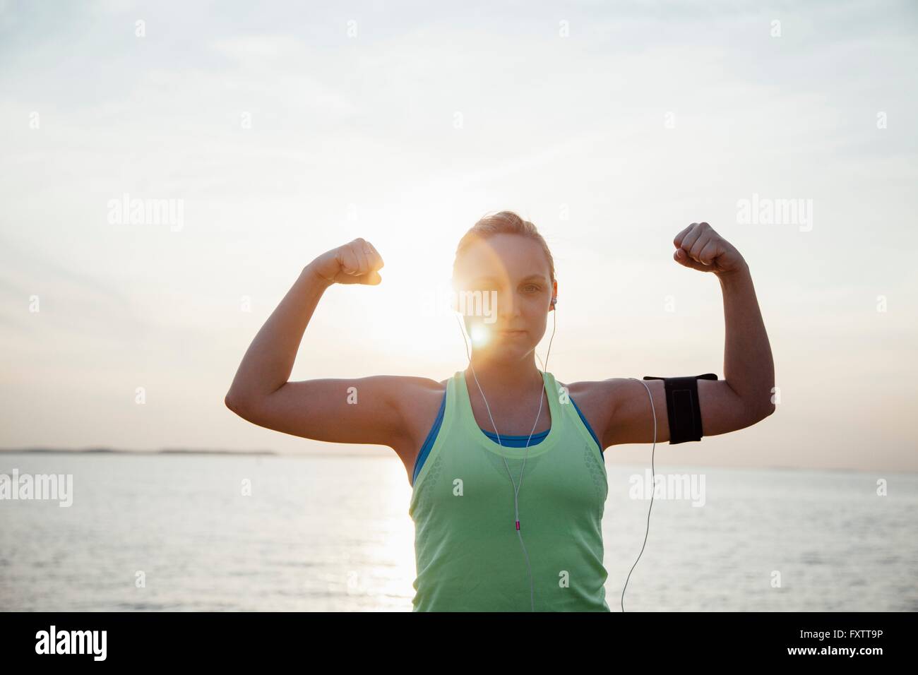 Woman wearing activity tracker, arms raised flexing muscles looking at