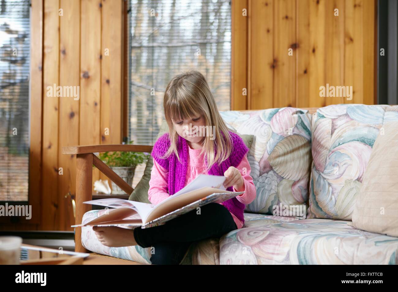 Girl sitting reading story book on living room sofa Stock Photo - Alamy