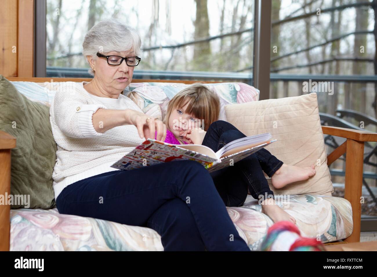 Senior woman reading story to granddaughter on living room sofa Stock Photo