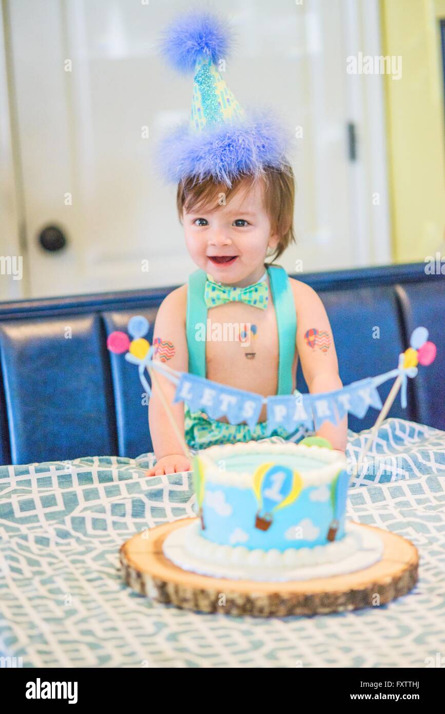 Baby boy wearing party hat with first birthday cake at table Stock ...