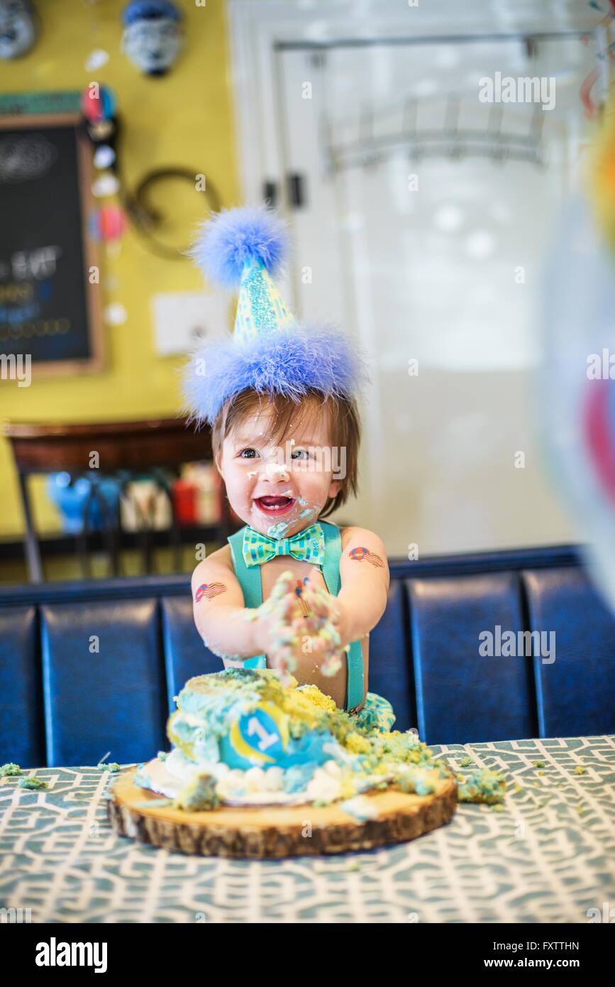 Baby boy wearing party hat smashing first birthday cake at table Stock Photo