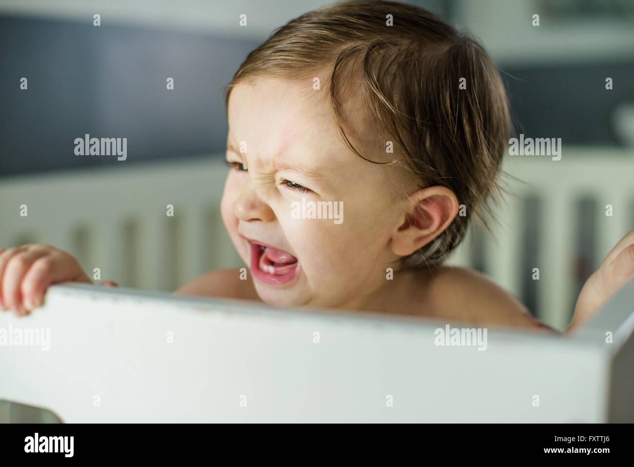Head and shoulders of baby boy crying in crib Stock Photo