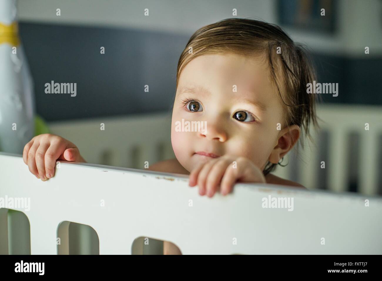 Head and shoulders of baby boy standing looking out from crib Stock Photo