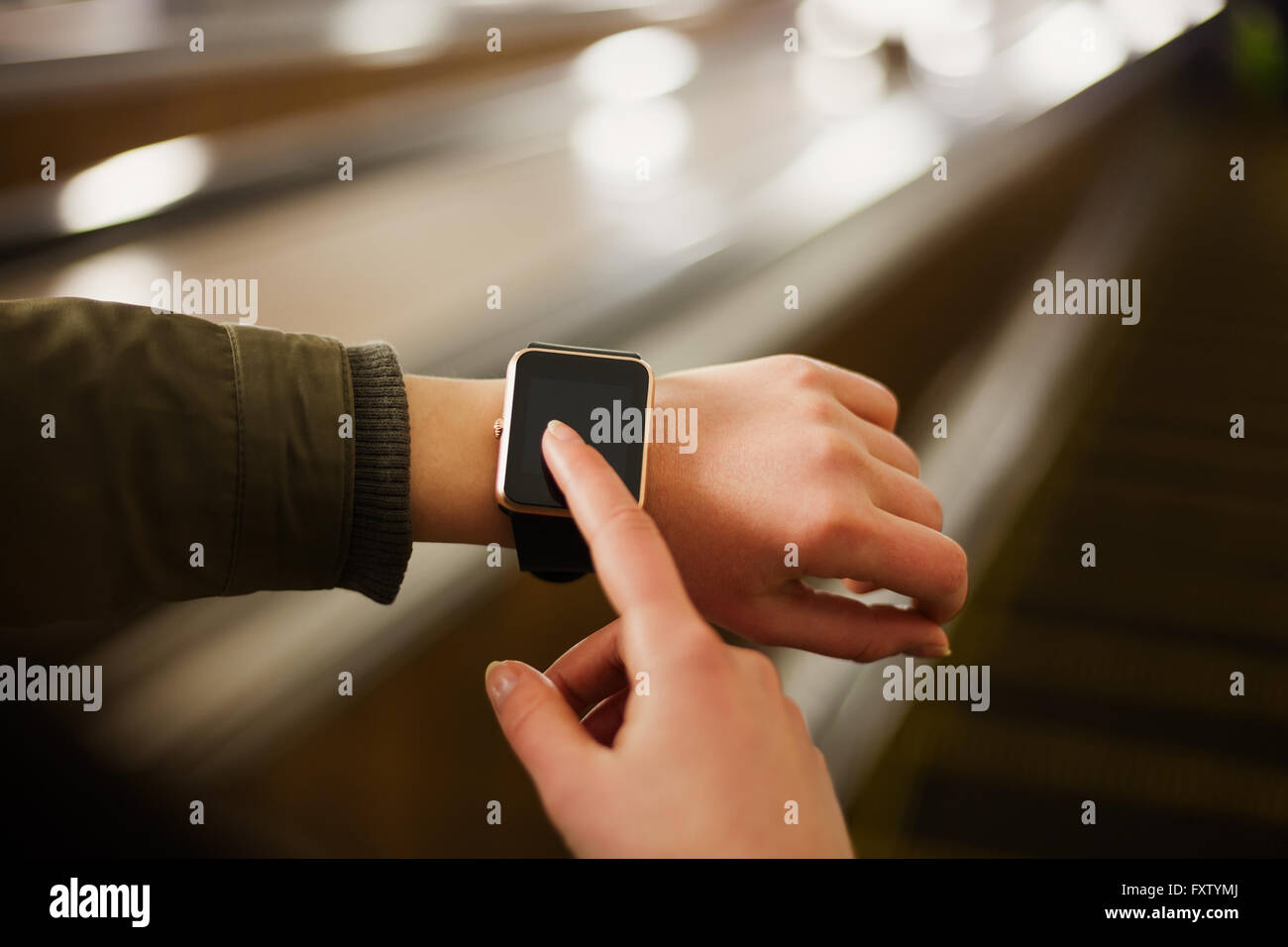 Woman using her smart watch while riding escalator in metro. This new device lets you always stay connected to internet and social media networks from anywhere you want. Stock Photo